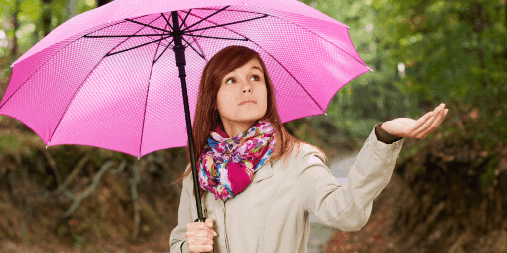 A woman stands in the rain, holding a colorful umbrella to shield herself from the downpour.