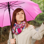 A woman stands in the rain, holding a colorful umbrella to shield herself from the downpour.