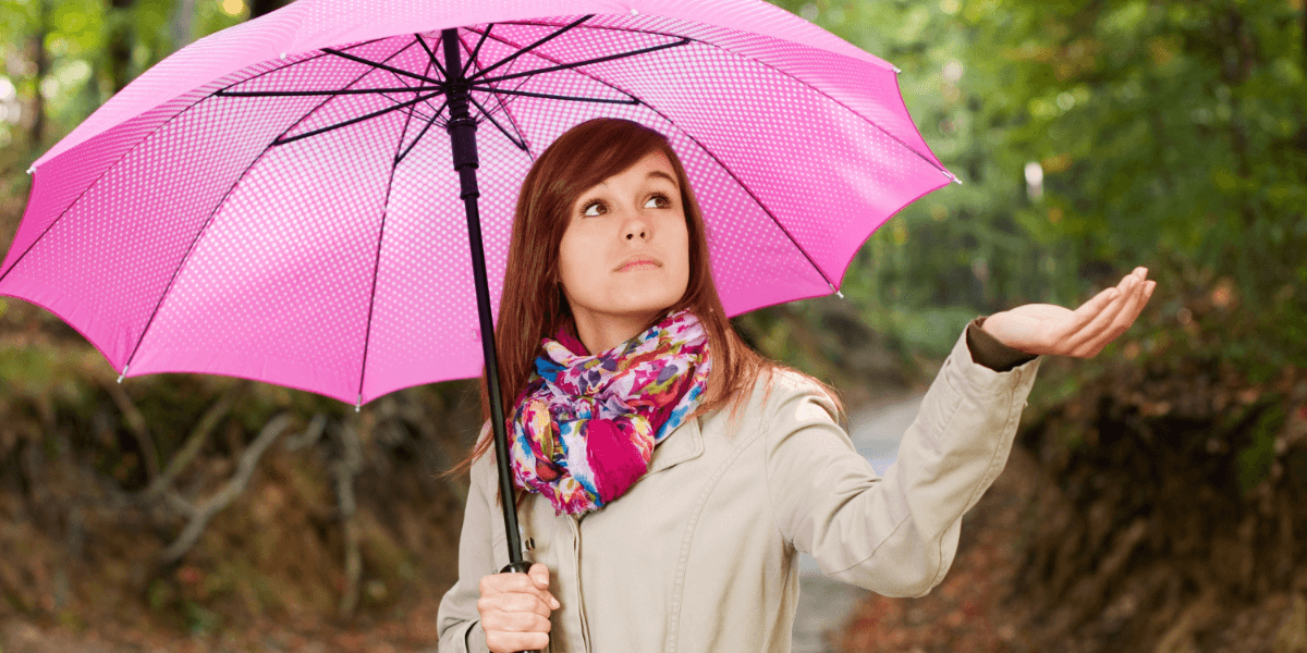 A woman stands in the rain, holding a colorful umbrella to shield herself from the downpour.