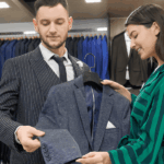 A man and woman examine various suits displayed in a clothing store, discussing options and styles.
